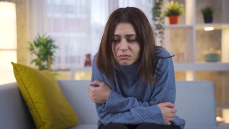 sad young woman sitting on sofa feeling unhappy, having unpleasant thoughts, suffering because of life problems.