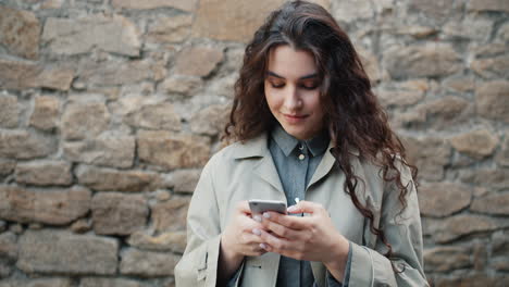 woman using phone outdoors near stone wall
