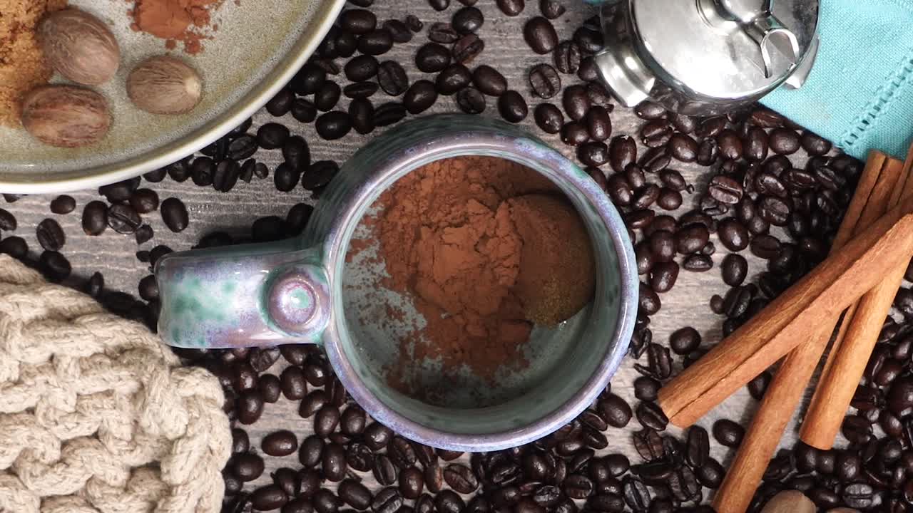 Cup or mug of coffee in a blue ceramic cup with whipped cream and a dash of nutmeg or cinnamon. Coffee beans surrounding a cozy cup of coffee in a blue mug.