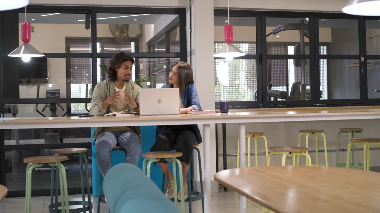 Diverse team man tapping laptop and woman watching, man flipping folder explaining plan in office