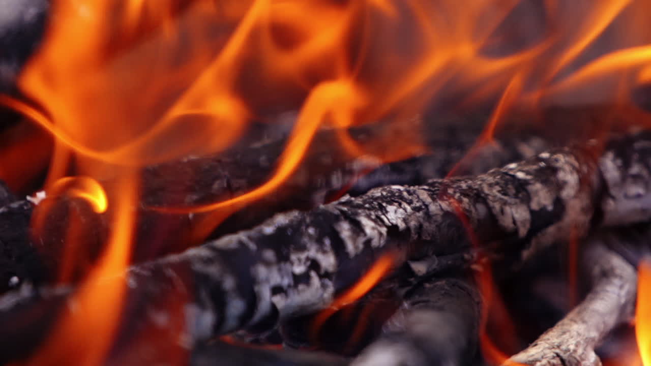 Motion of fire. Orange twisting tongues of fire. Wooden logs in flame. Smoldering logs in bright fire for barbeque. Wood on fire background. Macro shot. Slow motion.
