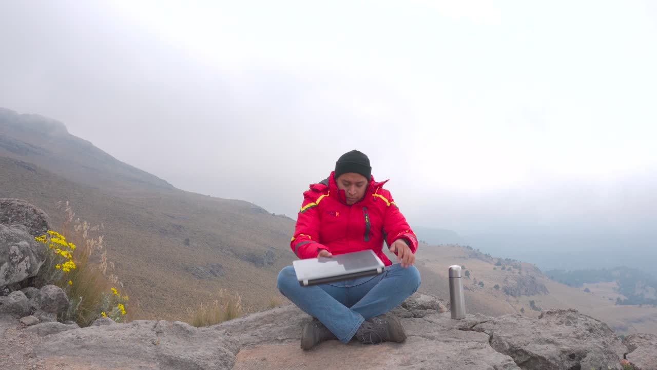 Young man sitting on a rock ad using a laptop and to drink coffe