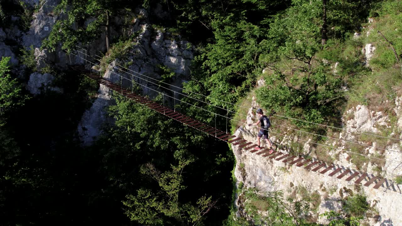 Scalatore che attraversa un ponte sospeso di legno su una via ferrata nelle montagne calcaree