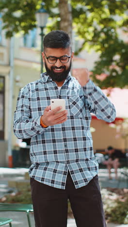 El-Hombre-Indio-Usa-Un-Teléfono-Inteligente-Móvil-Celebrando-Ganar-Buenas-Noticias-Al-Aire-Libre-En-Las-Calles-Urbanas-De-La-Ciudad