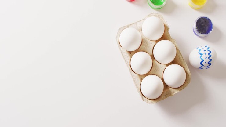 White eggs with colorful paints and brush on white background with copy space
