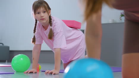 primer plano de una mujer entrenando a un niño pequeño que lleva un bloque rosa en la cintura durante una sesión de fitness, el niño intensamente centrado en la orientación del instructor
