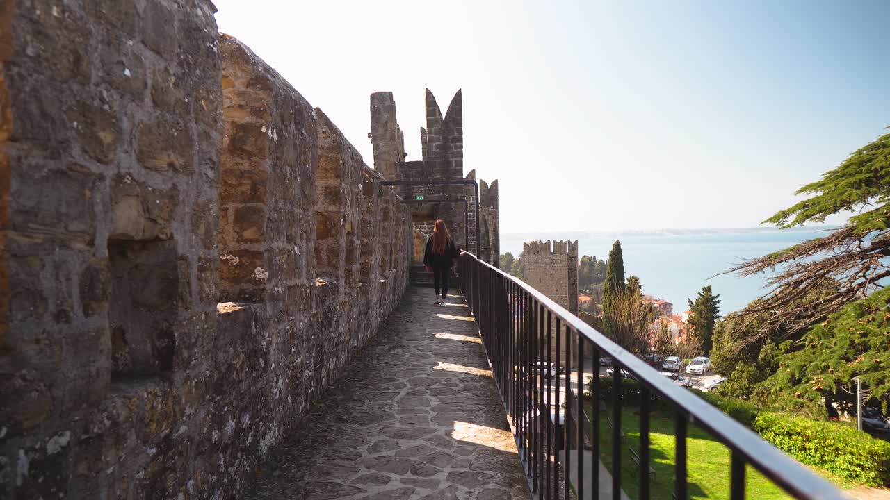 Young woman with long hair walking on stone ruins of castle with a view of the sea