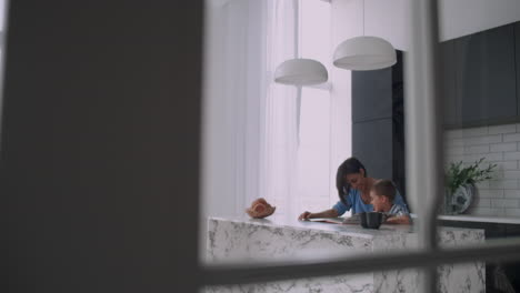 A-young-Spanish-mother-with-her-son-sitting-at-the-table-teaches-to-read-the-child-helping-and-prompting-his-son