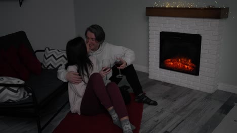 romantic young couple drinking red wine next to the fireplace