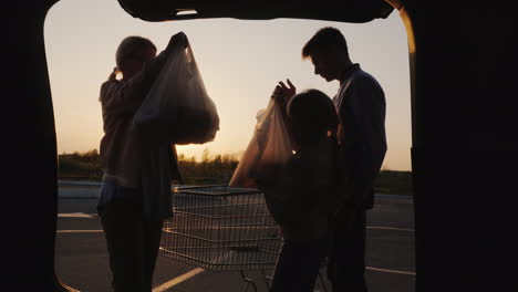 family puts shopping bags from supermarket in car boot