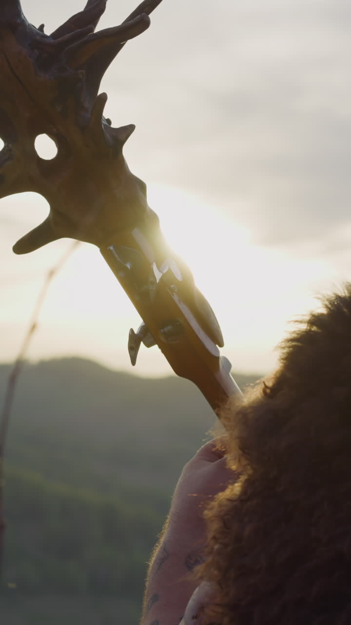 Man with dreadlocks and fur cape on shoulders plays tovshuur in valley close backside view. Art heritage of Siberian folks. Music sounds