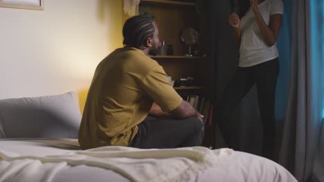 young couple relaxing at home at night with man sitting on bed talking to woman