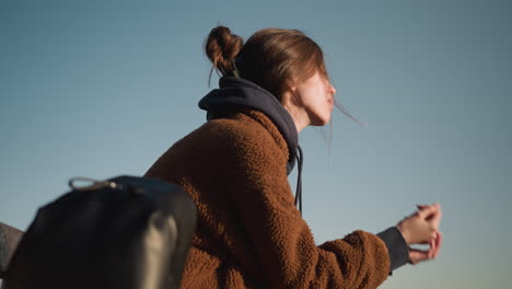 a close-up of a girl wearing a brown coat, with her hands covering her face, looking deeply worried and lost in thought. set against a clear sky background