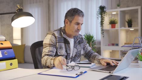 Mature-man-working-in-home-office-taking-off-his-glasses-and-working.