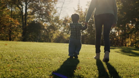 A-woman-walks-with-her-son-in-the-park,-leads-the-baby-by-the-hand