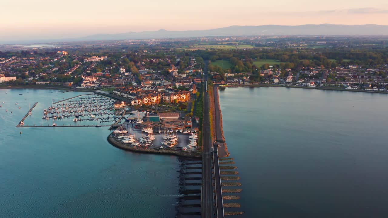 Aerial Reverse Shot of Dart Leaving Malahide Station Above Marina During Sunset