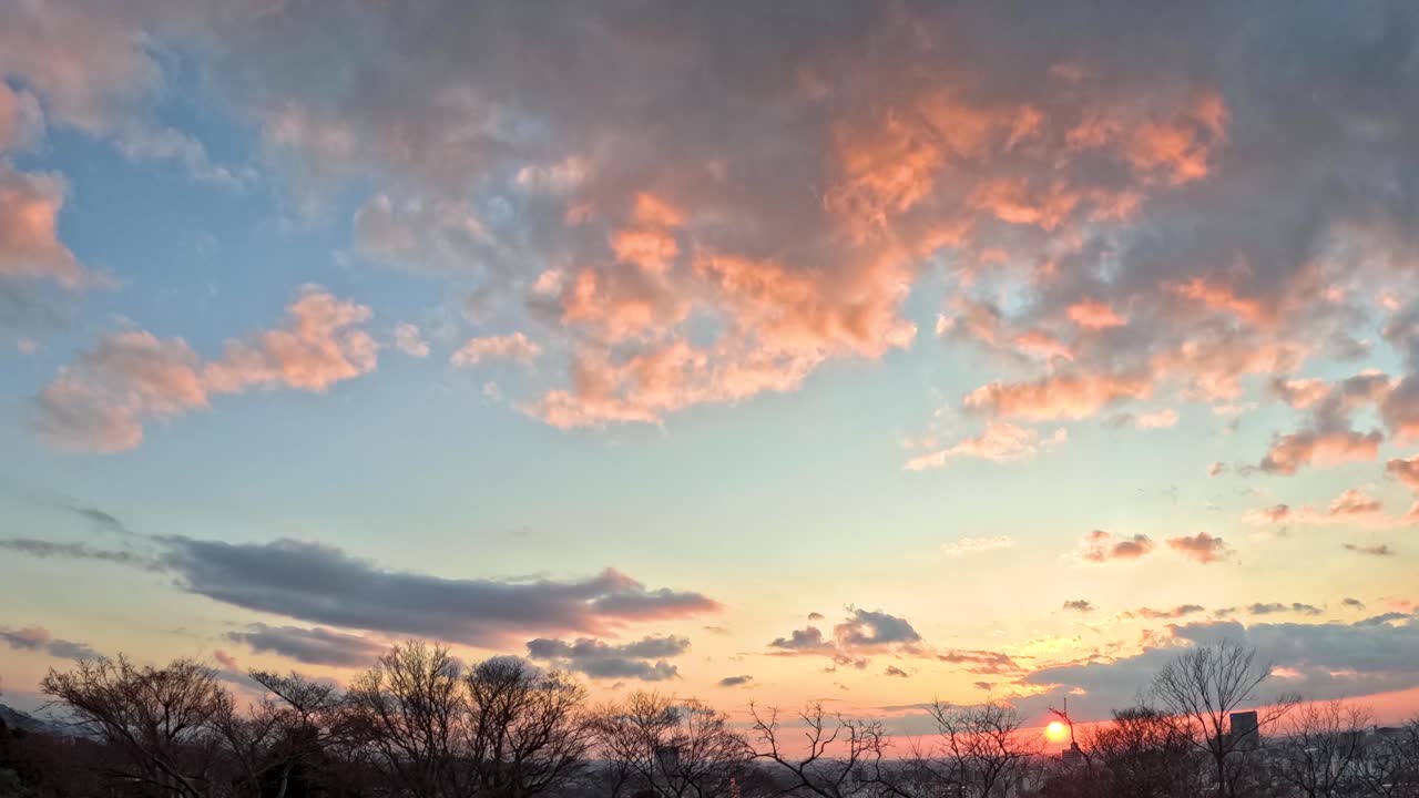 Static wide angle timelapse captures orange clouds moving across a sunset sky over Kanazawa