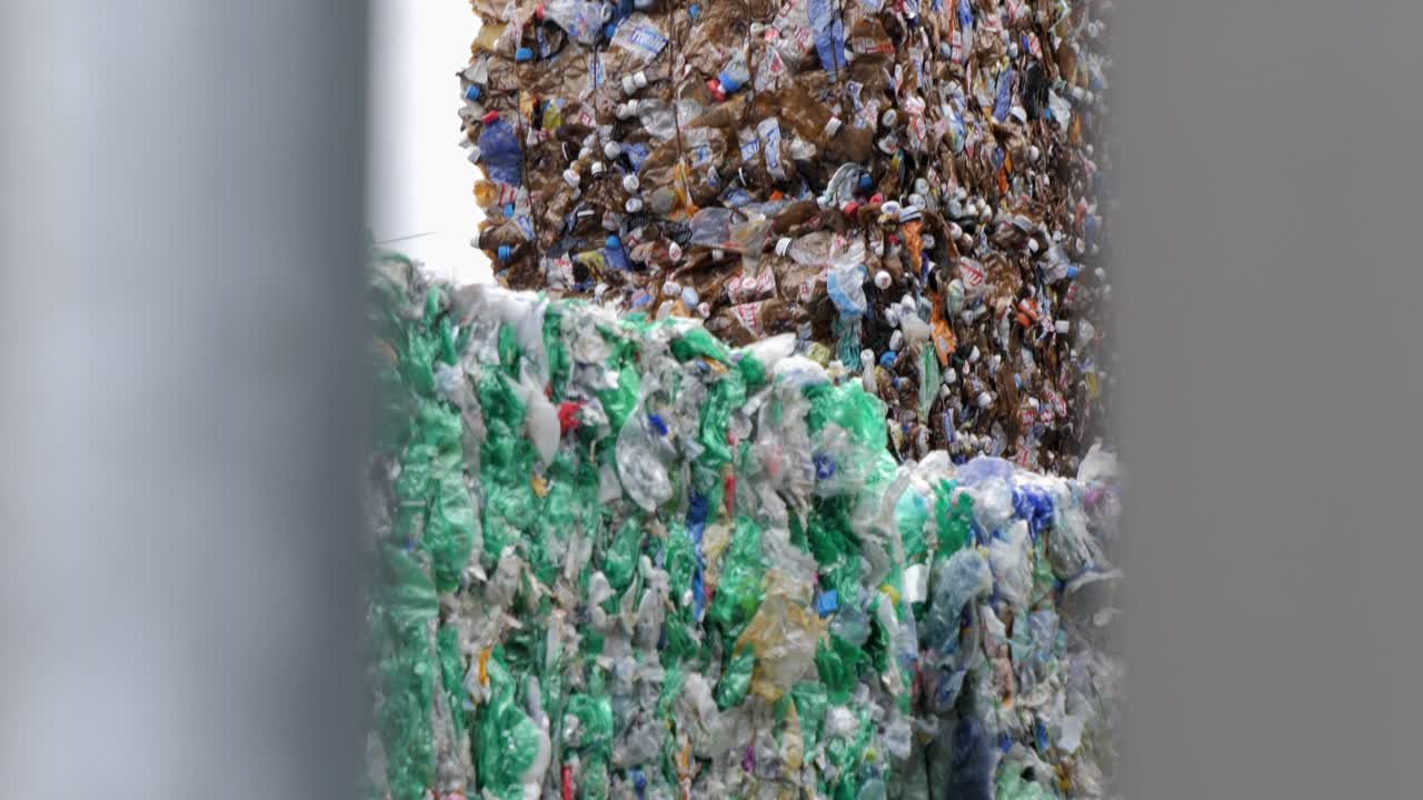 Stacks of crushed plastic bottles for recycling behind fence, boom down view