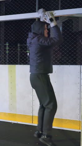 portero haciendo ejercicio con el poste de la portería durante la sesión de entrenamiento nocturno en la cancha deportiva al aire libre urbana, la escena incluye el enfoque en la preparación, edificios residenciales iluminados en el fondo