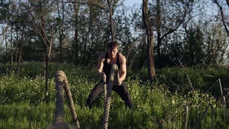 young fit man practicing in the park. he uses crossfit ropes for training. day time. sun shines