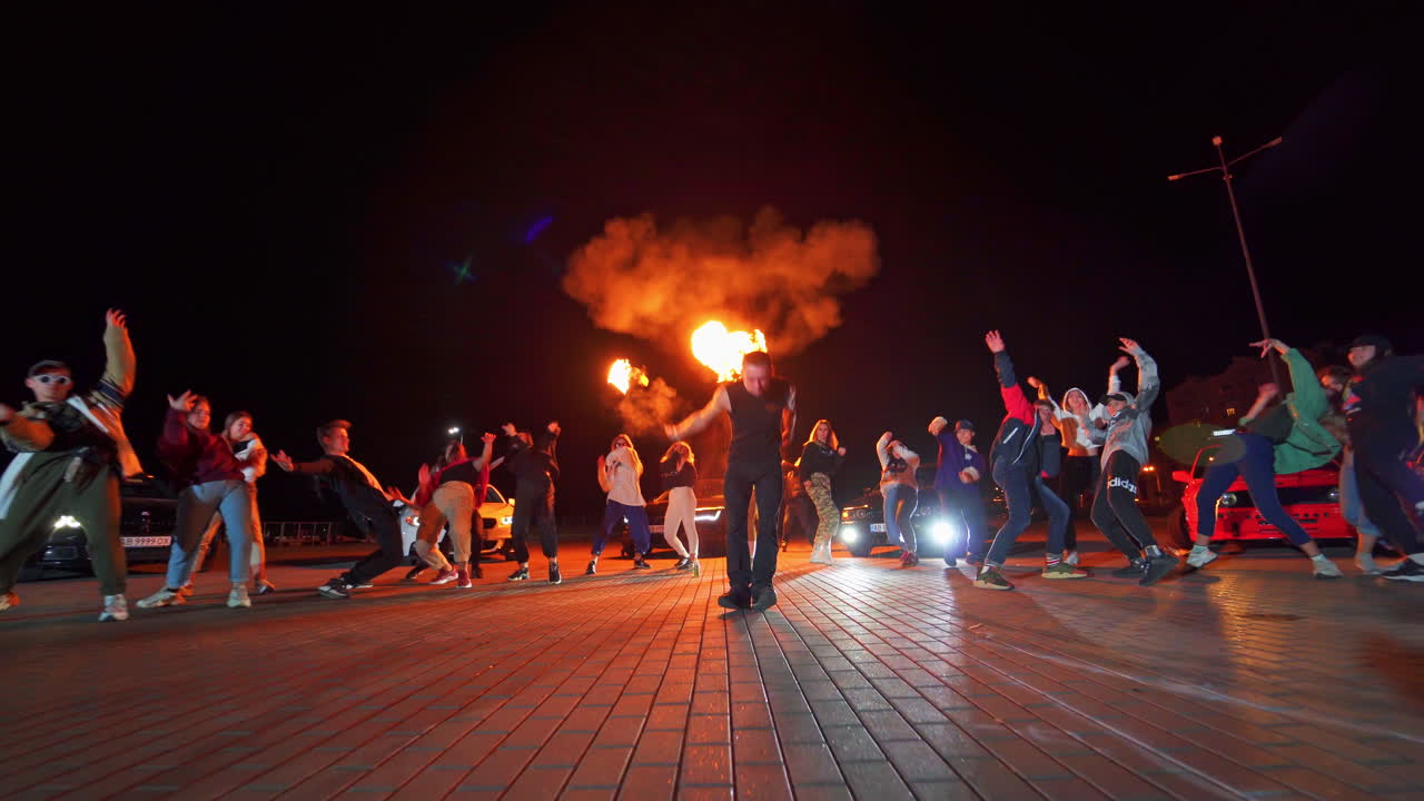 Hip hop party outdoors at night. Group of teenagers performing in stylish clothes. Man in the middle presents fire show.
