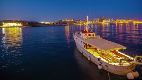 night timelapse of anchored boat in bay, valletta, malta, distant lights across bay