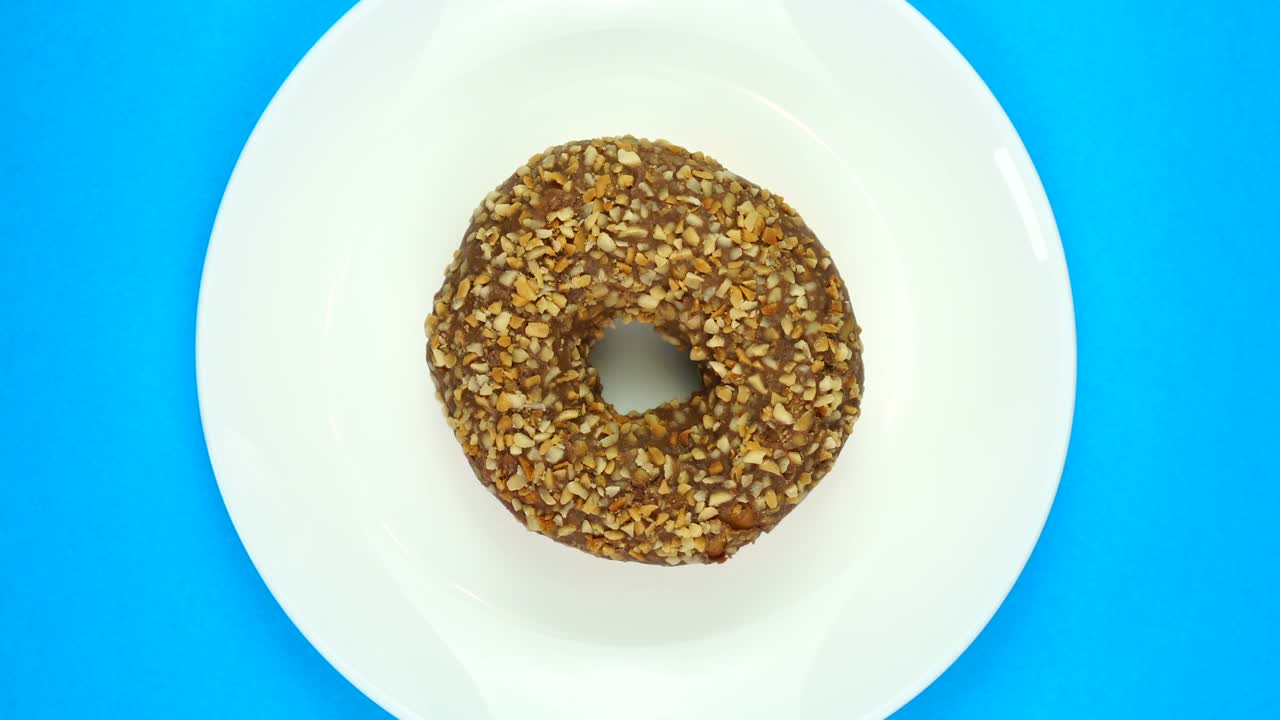 rosquilla de chocolate dulce horneada girando rápidamente en un plato. aislado en azul, vista superior