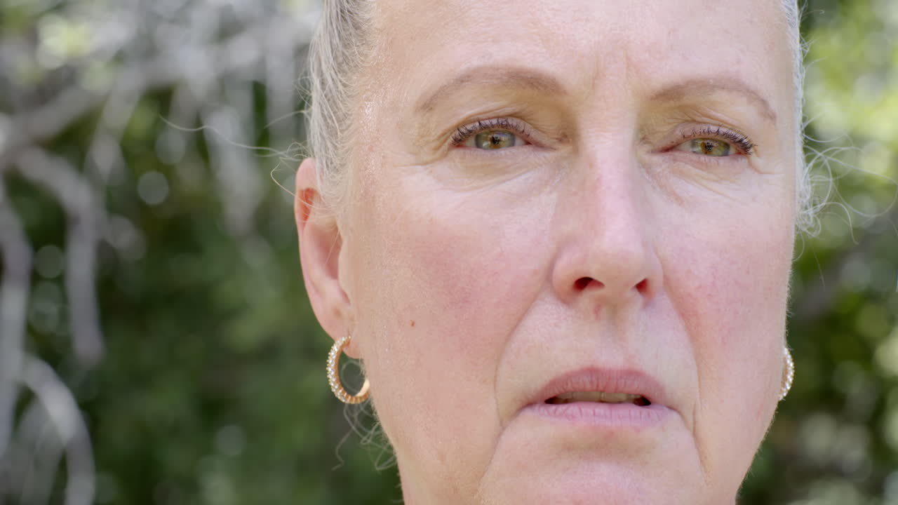 Oudere vrouw voelt zich tevreden in de tuin, lachend en omringd door de natuur, vrije ruimte voor tekst.