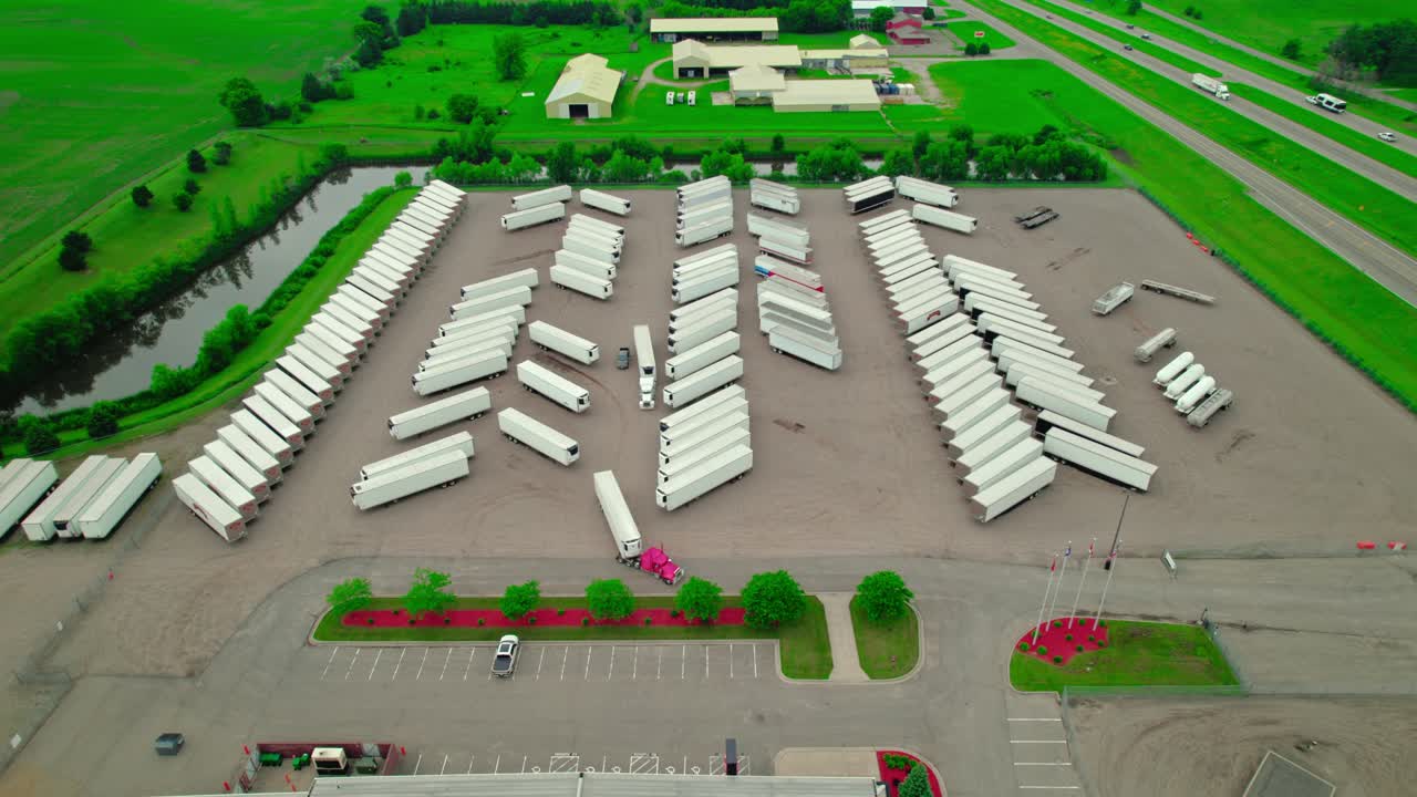 Aerial view of a parking lot filled with dry van and reefer trailers, with a red semi truck exiting. Minneapolis, Minnesota, USA