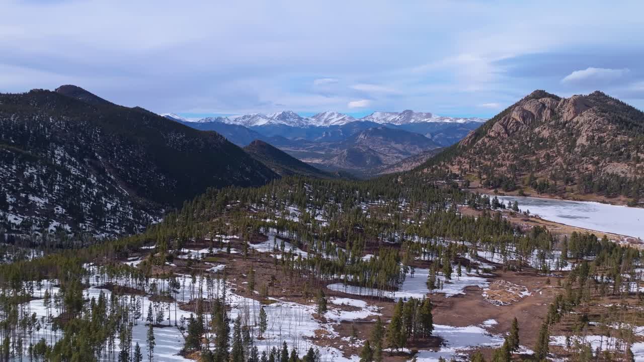 High aerial panoramic dolly over snowy ridge with sparse pine and dramatic rocky valleys below, Allenspark Colorado USA