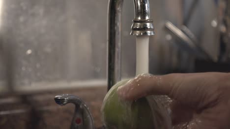 thorough cleaning of green apple using one hand on the kitchen sink