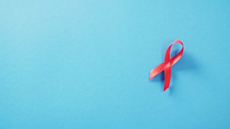 Video-of-red-hiv-or-aids-awareness-ribbon-on-blue-background-with-copy-space