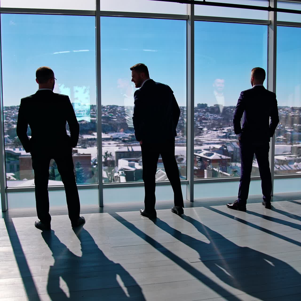 Funny businessmen in suits indoors. Office workers rest by the window. Business partners standing by the window and joyfully moving their bodies. Back view