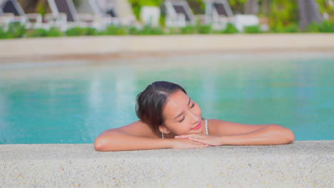 close-up of a pretty young woman resting her head on the arms along the edge of a resort swimming pool