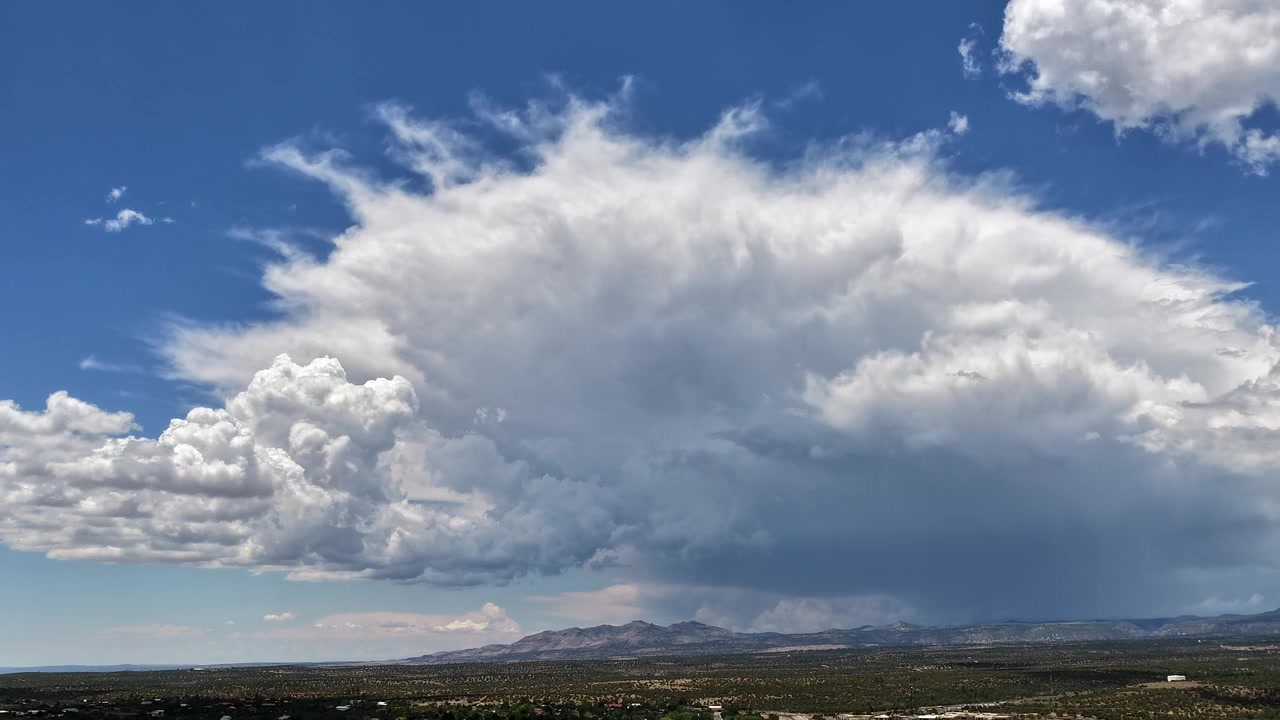 4K drone timelapse of a massive cumulonimbus monsoon storm system dispersing with a heavy rain shaft over a vast Southwest high desert mountain landscape against a blue sky.