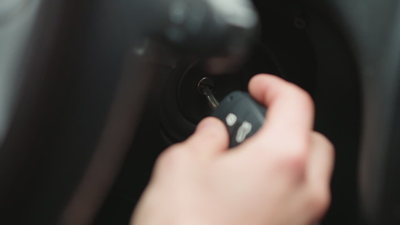 Close up of road traveler inserting metal key into ignition starter and turning key inside vehicle cabin focusing on hand movement dashboard detail and winter jacket sleeve before engine start