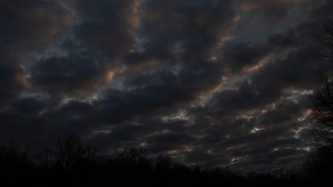 Gray clouds pass over silhouetted hills at sunset - 4K Timelapse