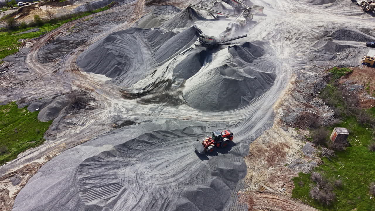 Granite quarry site shows activity with machinery working and rock piles in different shapes during daytime hours