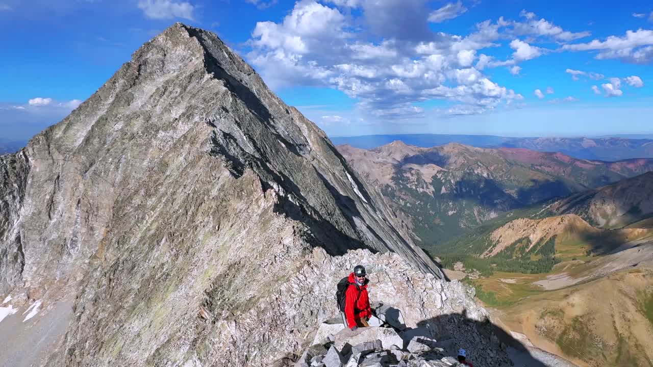 Hiking Capitol Peak Wilderness Knifes Edge North East Ridge Trail scrambling rock climbing Rocky Mountains Colorado 14er boulders summer blue sky morning sunny rugged terrain pan left