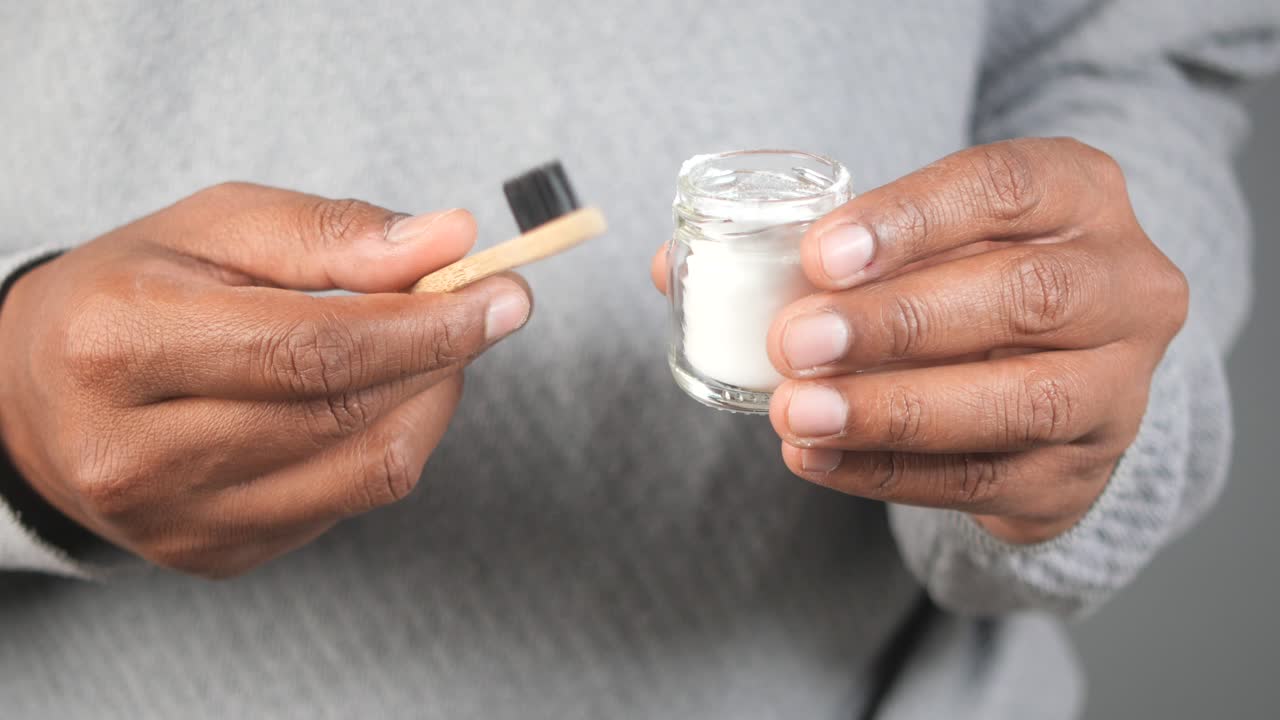 Hands holding a bamboo toothbrush and a small glass jar of natural tooth powder
