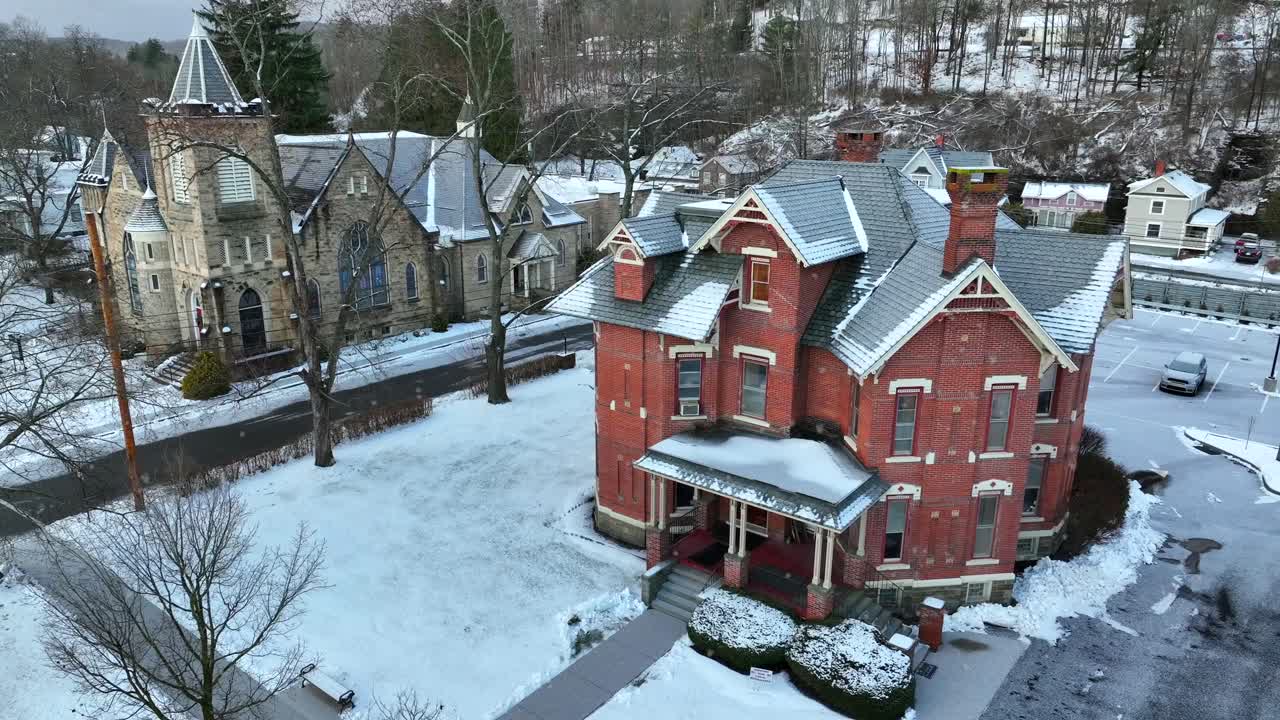 cámara aérea lenta de la casa victoriana y la iglesia durante la tormenta de nieve