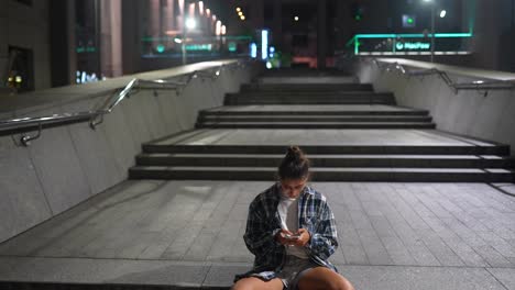 joven usando un teléfono inteligente en las escaleras de la ciudad por la noche