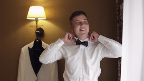 groom man adjusts bow tie, preparing to go to the bride, businessman in white shirt, wedding day