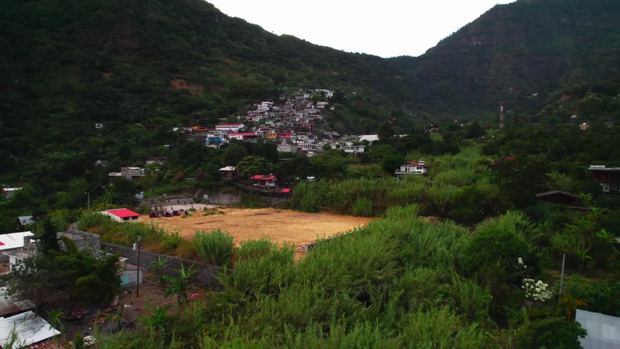 Drone panorâmico à direita seguindo o litoral acidentado e as encostas das montanhas do Lago Atitlán sob a luz quente do sol