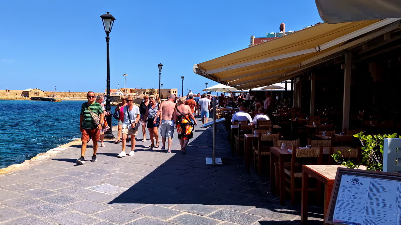 Tourists and foreigners walking along a ridge of the coasts and beaches of Chania in Crete, Greece next to restaurants
