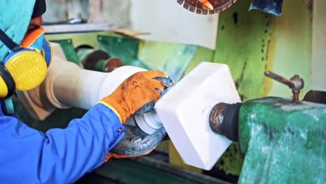 worker man in special uniform with mask polishing stone in workshop.