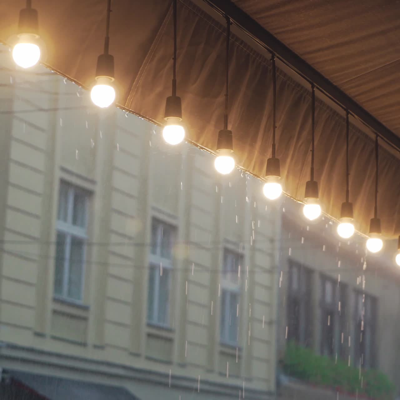 view on a row of burning light bulbs from the roof of a restaurant on the background of raindrops from the street. It's raining