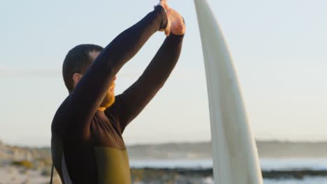 vista lateral de un surfista caucásico adulto estirándose y calentándose antes de surfear en la playa 4k