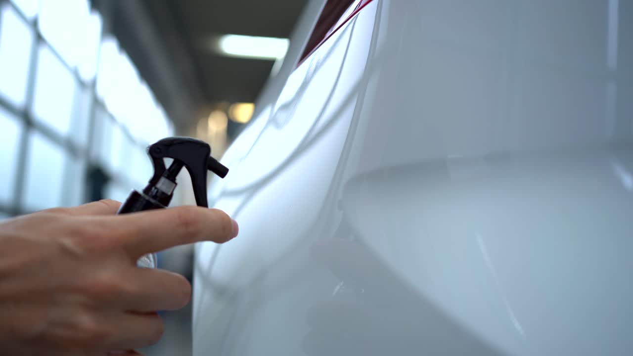 Una persona sta spruzzando acqua su una vernice fresca bianca di un'auto. Gocce d'acqua stanno cadendo dalla superficie. L'auto è una Volkswagen bianca. La superficie è stata lucidata. Questo dimostra il nano-rivestimento di una superficie.