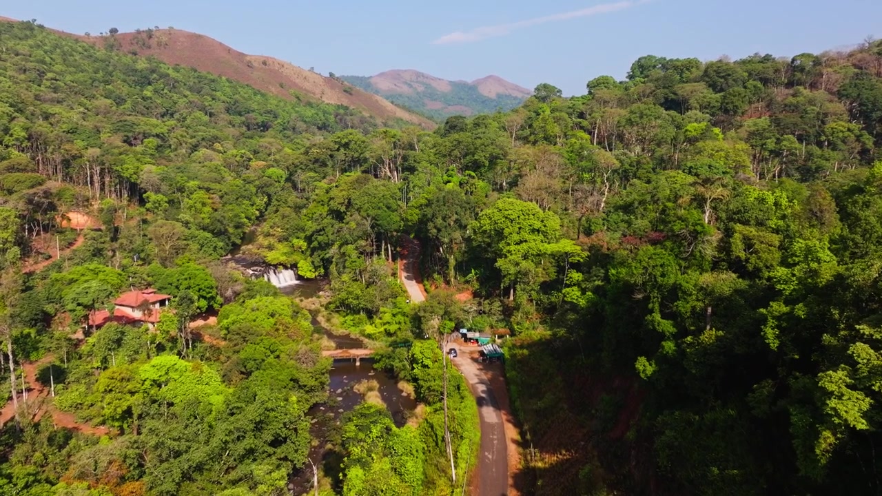 Luftfoto af Kote Abbey-vandfaldene med Kote Betta, træer, smal vej og et fritliggende hus ved Mukkodlu, Coorg, Madikeri, Karnataka, Indien. Dagtimerne, indzoomning, droneoptagelse, 4K.